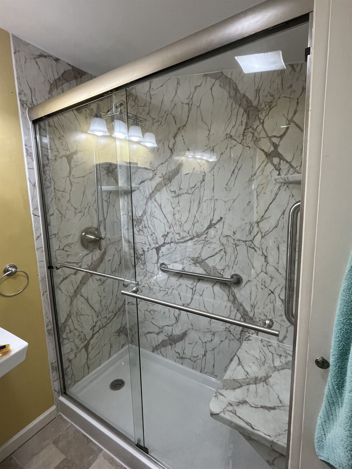 Marble look acrylic walk-in shower with sliding glass doors and grab bars