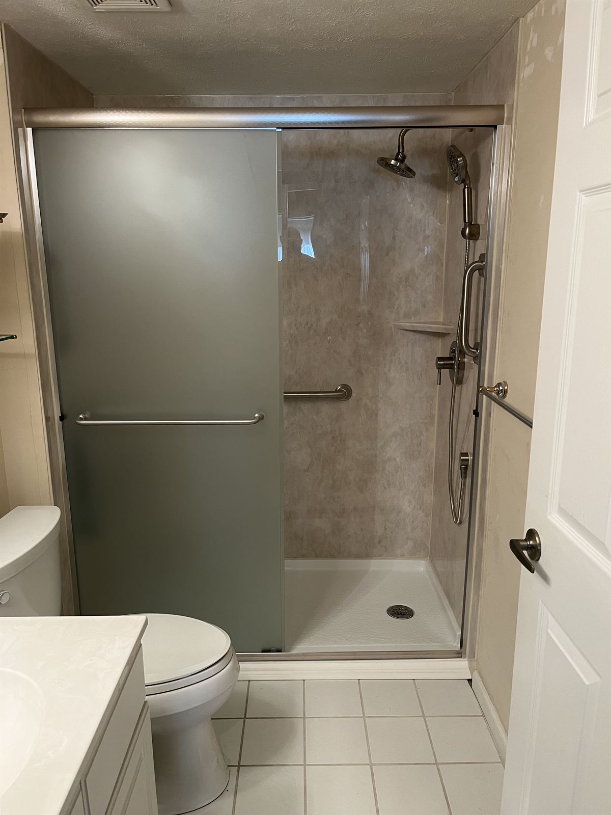 Travertine look acrylic shower with frosted glass sliding doors and dual shower heads