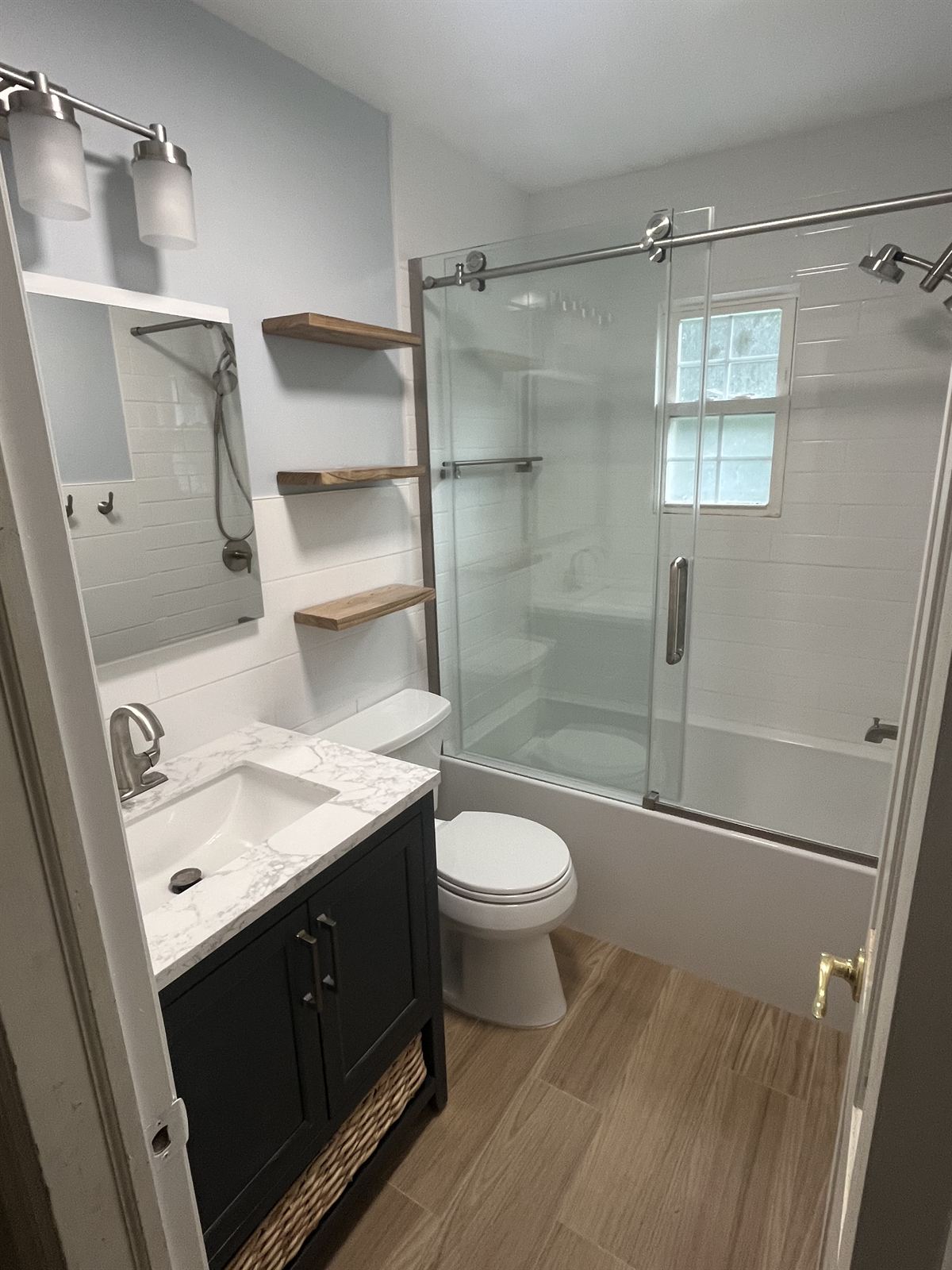 After: custom tile shower with subway tile walls, modern sliding glass door, charcoal vanity and wood look floor