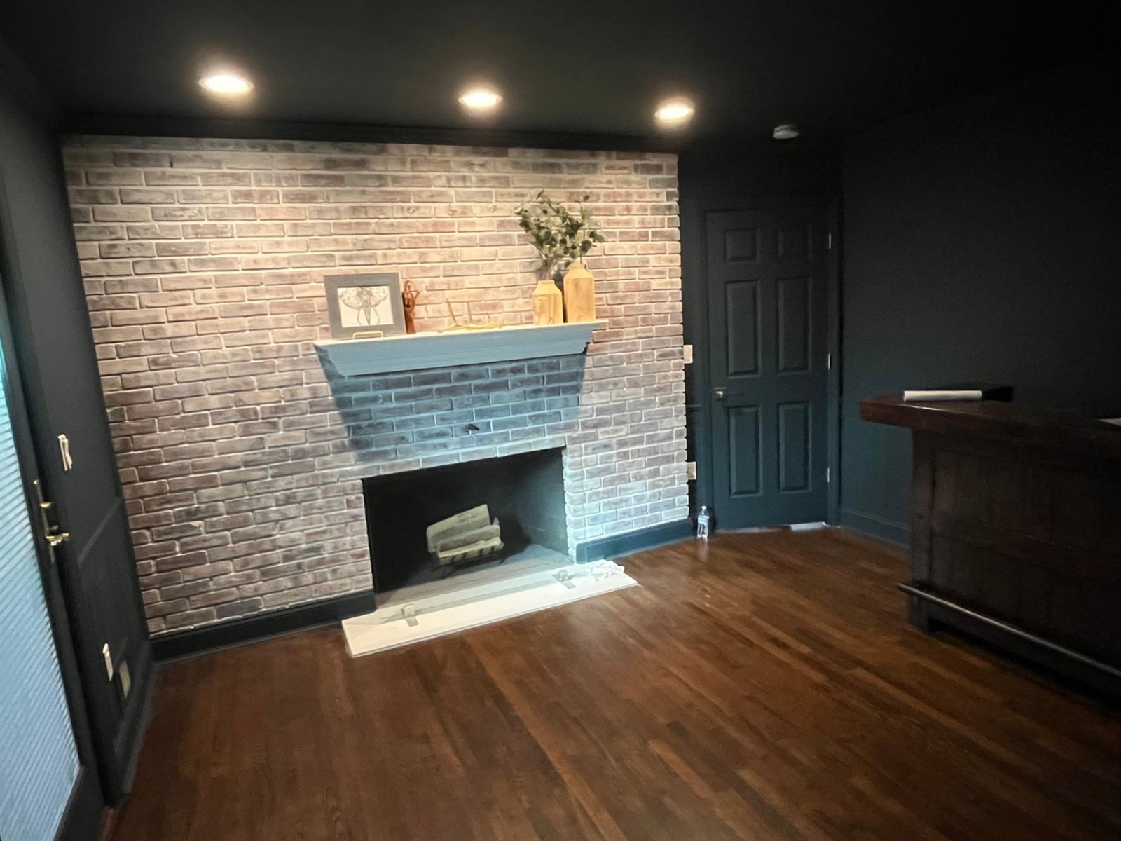 After: the den with the stairs gone, a new wall, deep charcoal paint, and a whitewashed brick fireplace