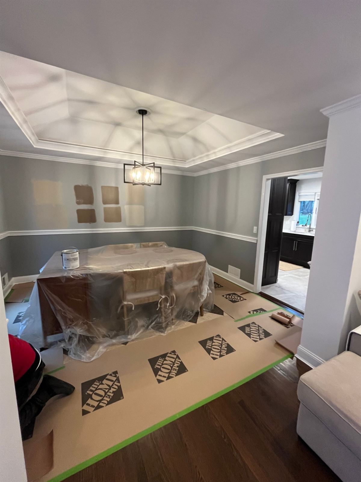 Before: the same dining room with paint swatches on the wall, furniture wrapped and floors covered