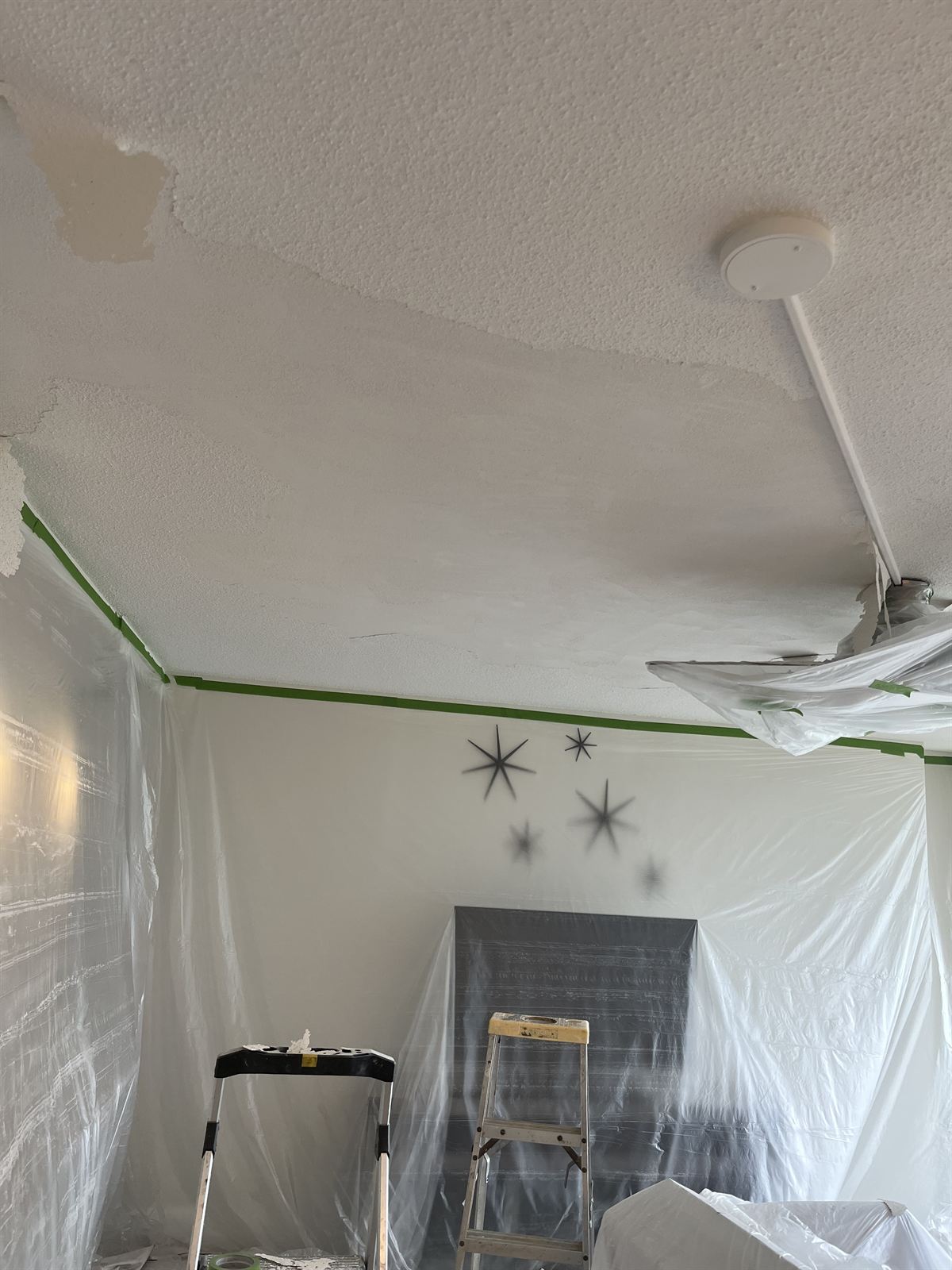 Before: popcorn ceiling half scraped, with the whole room masked in plastic