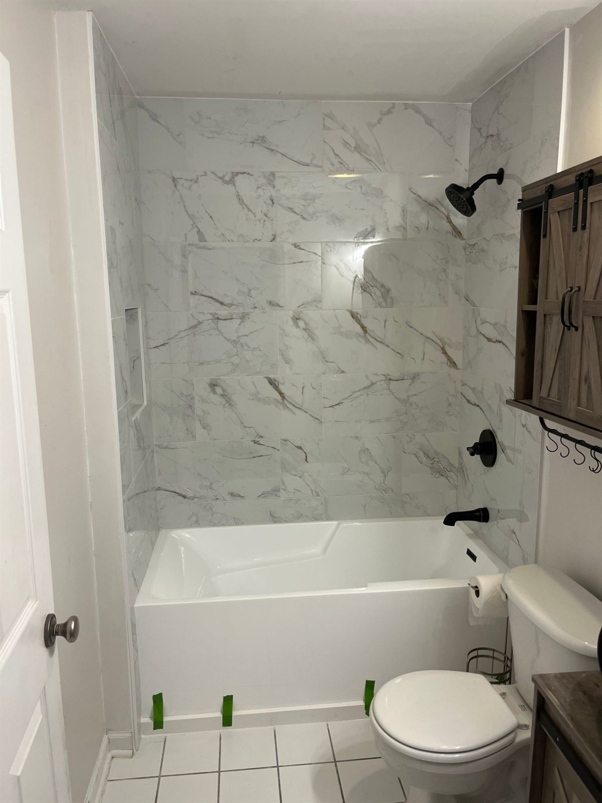 After: marble look tile tub surround with recessed niche and matte black fixtures